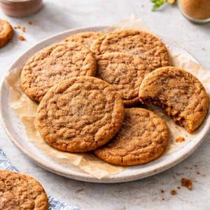 A plate of large soft ginger cookies with a crackly sugar top, one cookie bitten to show the chewy center.