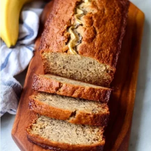 Sliced banana bread on a wooden cutting board with ripe bananas