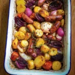 Pink potato and sausage tray bake served with fresh herbs