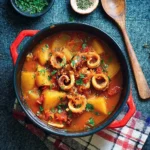 Bowl of Portuguese potato and squid stew garnished with fresh herbs