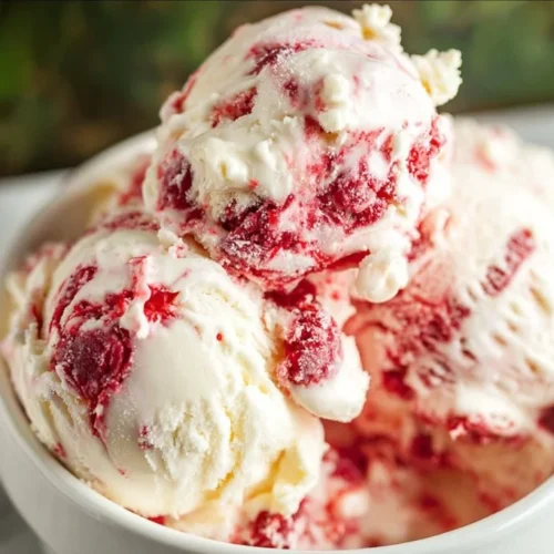 A bowl of Raspberry White Chocolate Chip Ice Cream topped with fresh raspberries and white chocolate chips.