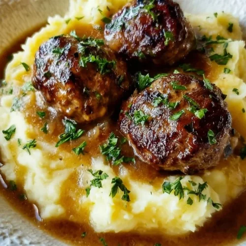 Salisbury steak meatballs served with garlic herb mashed potatoes on a plate.