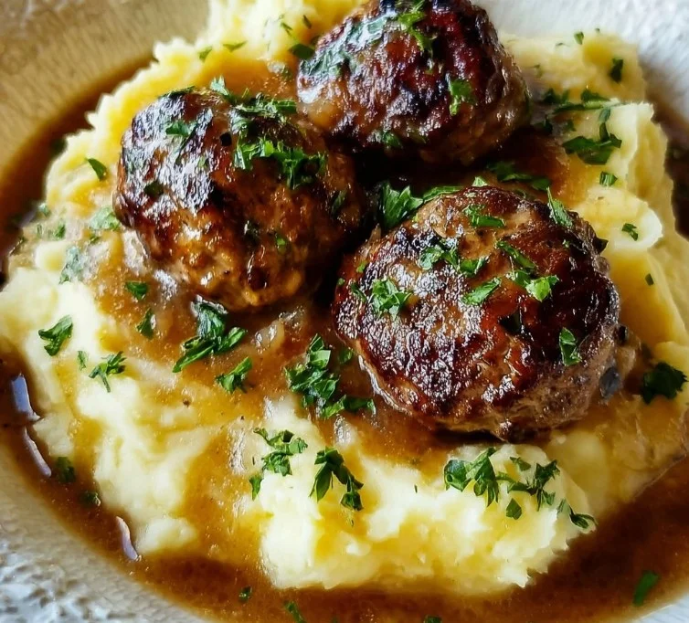 Salisbury steak meatballs served with garlic herb mashed potatoes on a plate.